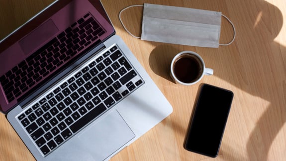 Laptop, coffee, cell phone, and facemask on a desktop.