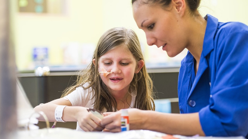 A volunteer helps a girl glue something on a piece of paper.